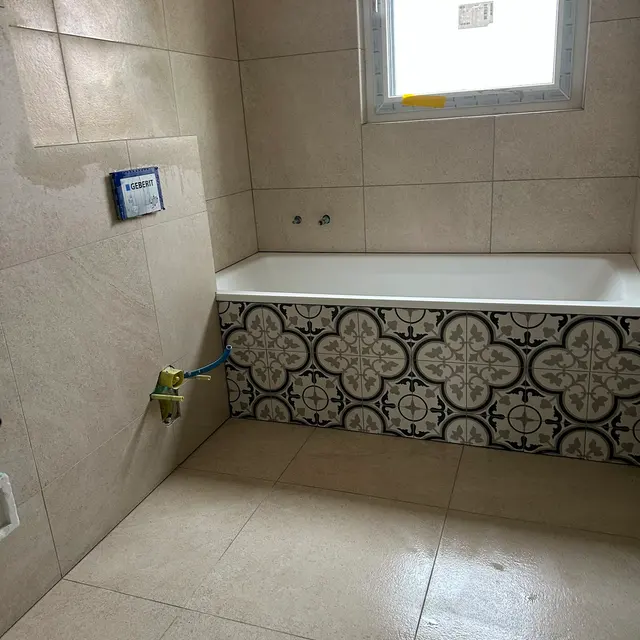 Bad mit Badewanne: Wand und Boden in hellem Grossformat, Wannenverkleidung mit Ornamentplatten