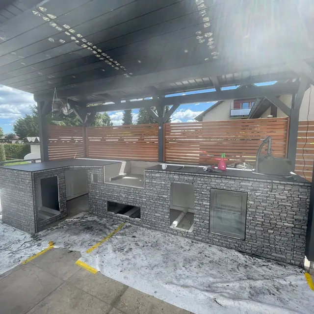 Sitzplatz mit Outdoor-Küche: Grossformatige Terrassenplatten unter der Pergola, rund um die Aussenküche verlegt
